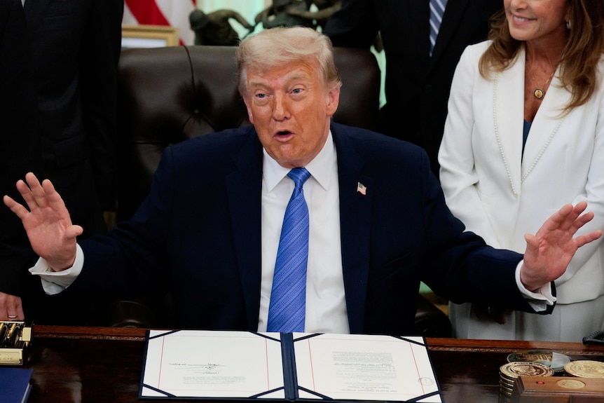 Donald Trump sits in the White House, with his hands up gesturing while talking.