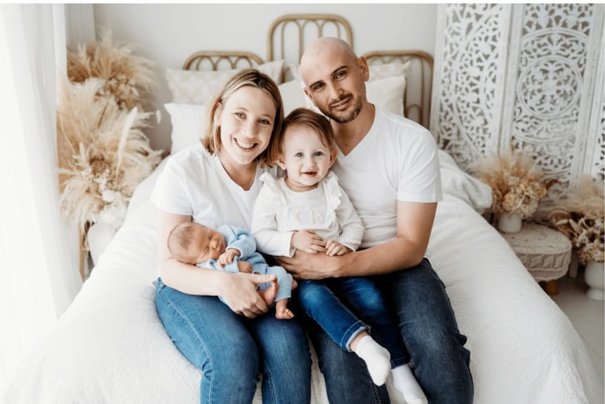A family including two adults, a baby and a toddler pose together.