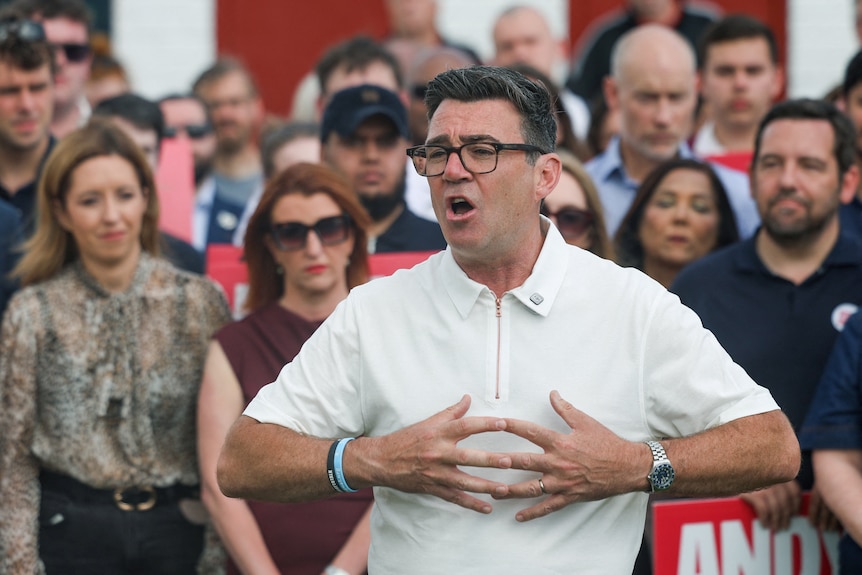 A dark-haired, middle-aged man in glasses animatedly addresses a crowd.