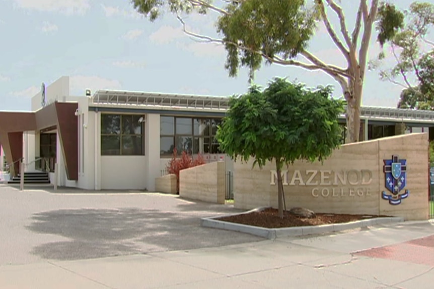 White and brown buildings stand behind a sandstone gate with a large emblem and writing that says "Mazenod College".
