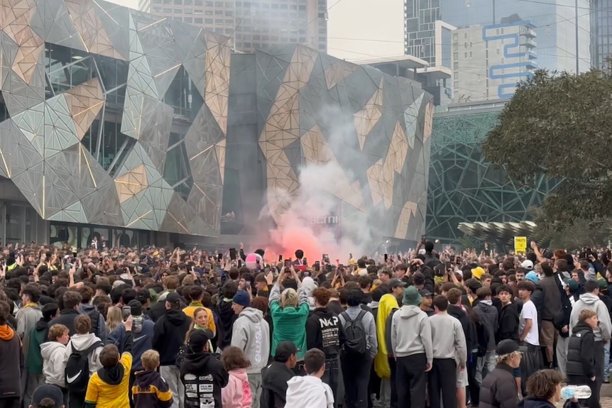 A large crowd gathered with a smoky red haze coming from the front after a flare was lit.