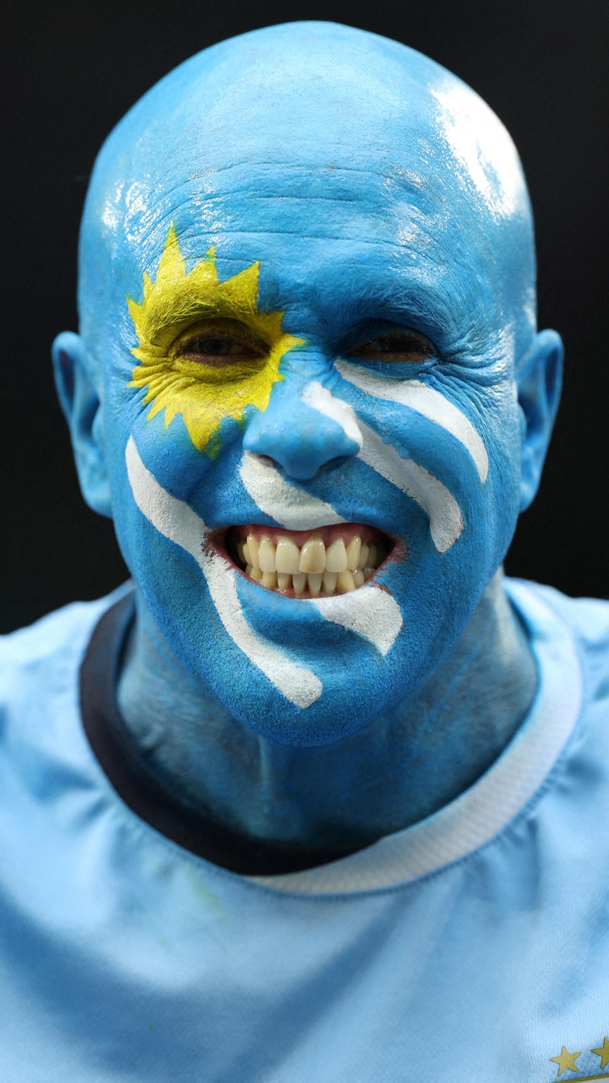 a portait shot of a man with bright blue facepaint with a yellow star and white stripes