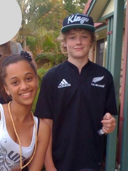 A school-aged girl wearing a white singlet and a boy wearing an All Blacks jersey smile at the camera.