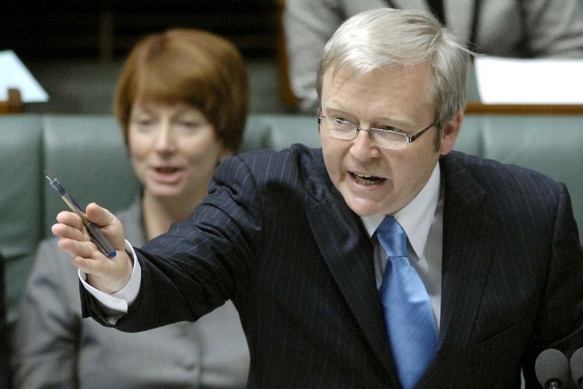 Ken Rudd, wearing a dark suit, gestures with his right hand while holding a pen. Julia Gillard is in the background.