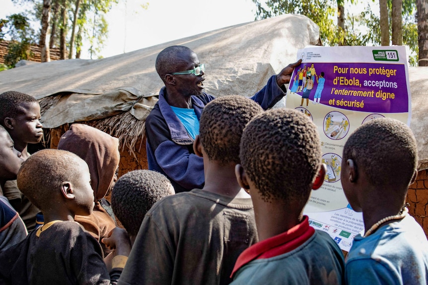 A man holds up an information sheet about Ebola as he gives an information session to children and teenagers.