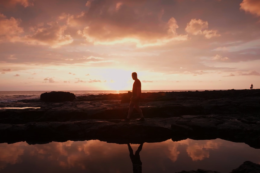 Marc walks over rocks at sunset in a Hawaiian bay.