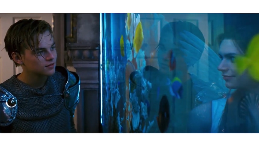 A screenshot from a film shows two characters looking at each other through the glass of a fish tank.