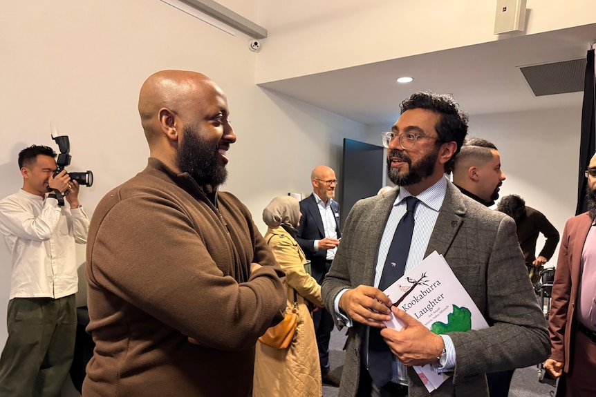 Two middle aged Middle Eastern men stand and talk in a room