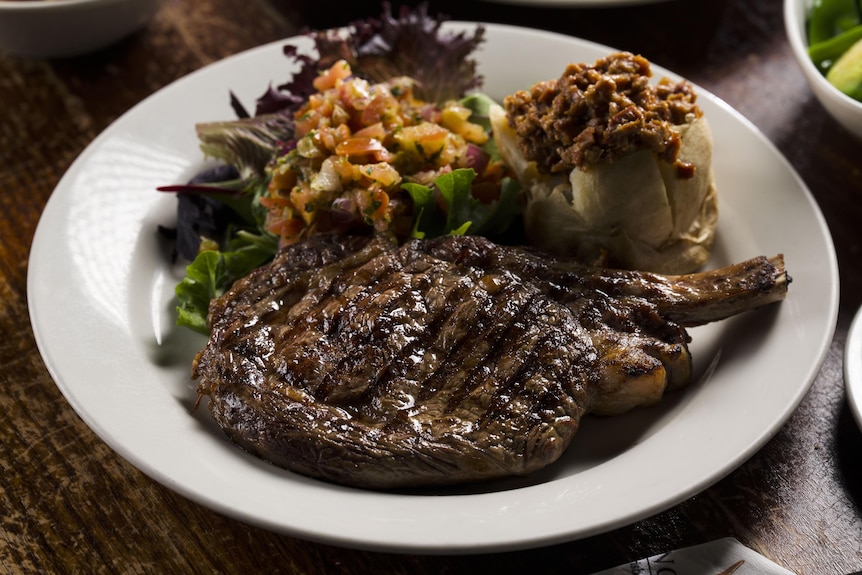 A juicy rib steak on a bone served on a restaurant plate with a sophisticated salad and glaze.