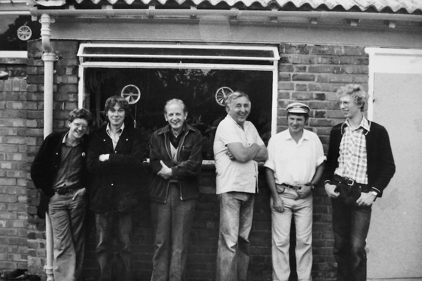 Black-and-white photo of six men smiling and standing in front of a brick building, a young blonde Jerry on the right