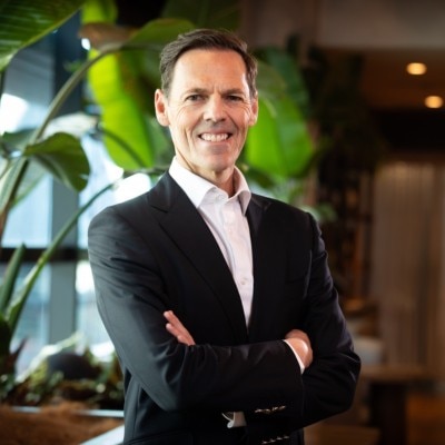A man wearing a suit jacket and white shirt standing in front of large plant leaves