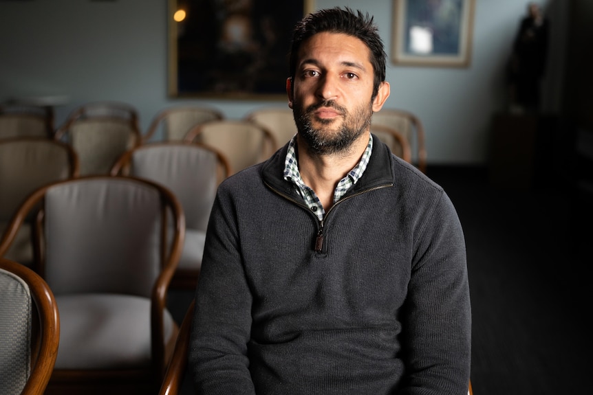 A man sitting down in a room full of rows of chairs.