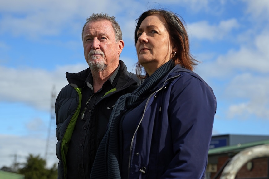 A man and a woman stand leaning on a low fence at a sports oval.