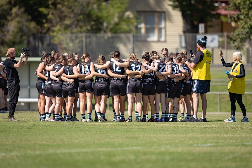 A team of female footballers stand with their arms around each other.