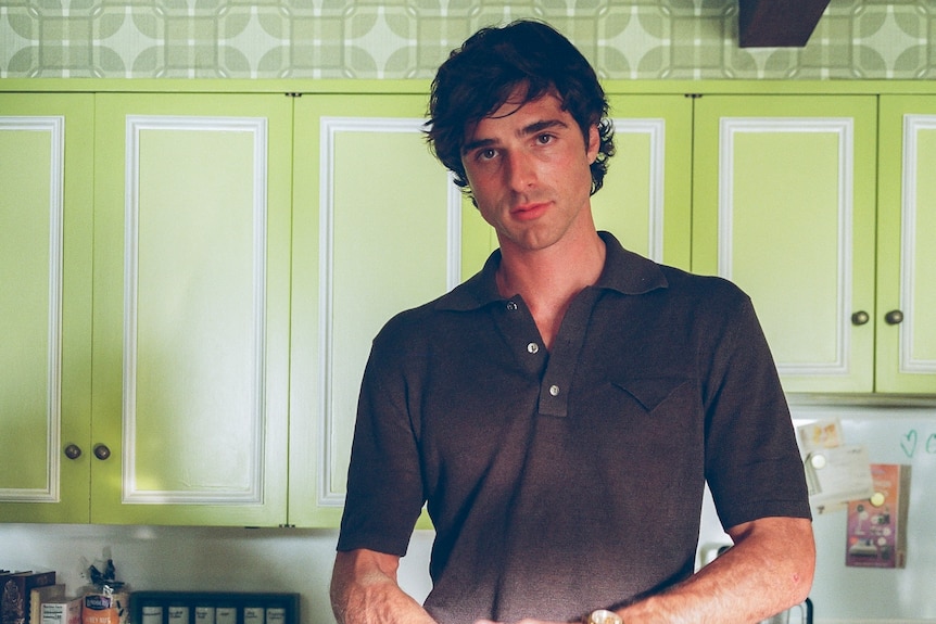 Jacob Elordi standing in a kitchen holding raw meat over a bowl as if cooking