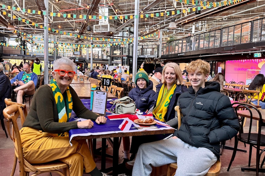Two women and two teen boys in socceroos scarfs sitting at a cafe table