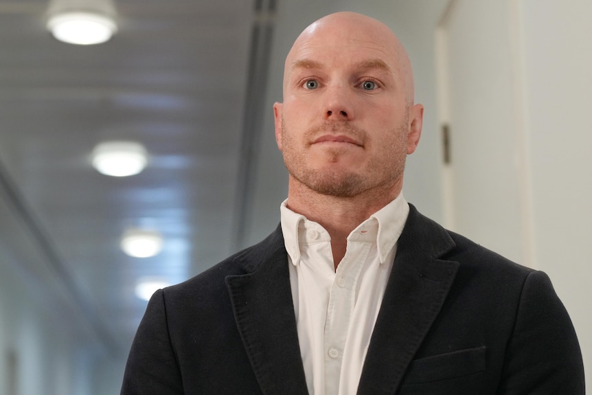 a young bald man wearing a suit in a hallway.