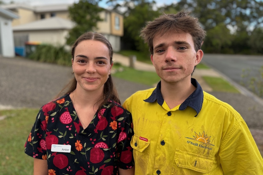 A young woman with dark hair and a young man in hi-vis shirt, standing in a suburban street.