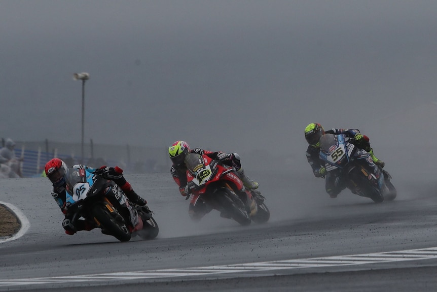 A line of three World Superbike riders driver round a corner through the rain.