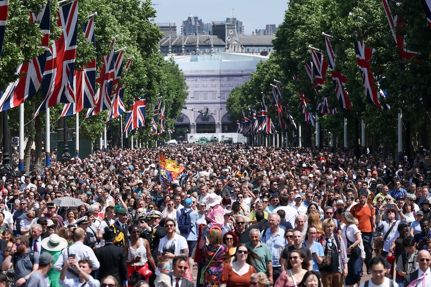 A huge crowd of people gathered near Buckingham Palace in London, with big British flags displayed on banners