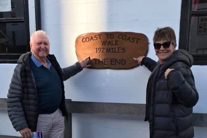 A man and a woman pointing to a wooden sign