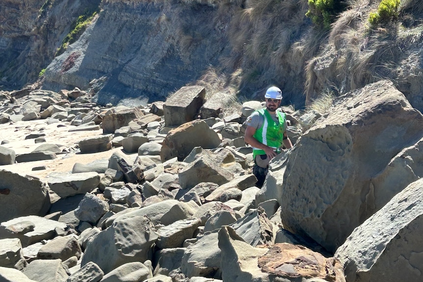 Man in hi-vis gear standing among coastal rocks.