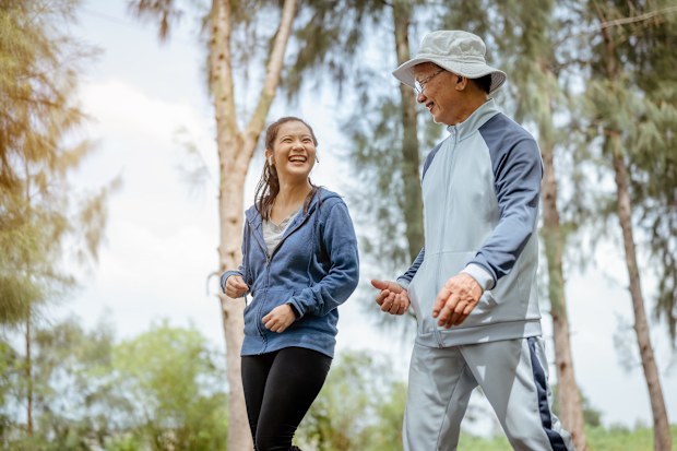 A woman and grandfather are walking jogging on the street at the park.