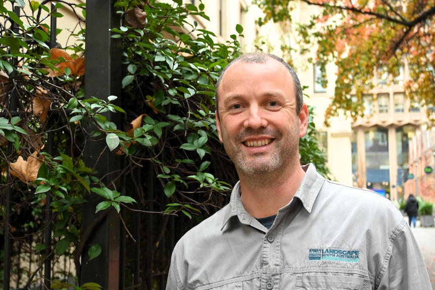 A man stands next to a bush in a shirt branded with the Kangaroo Island Landscape Board logo