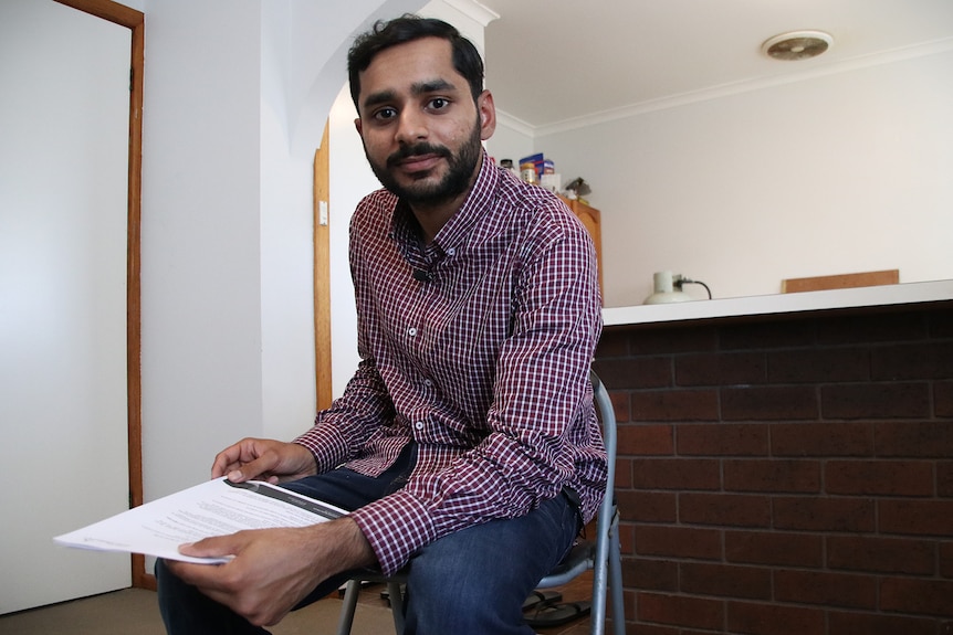 Miftah Ud Din sits near his kitchen, holding a printed letter.