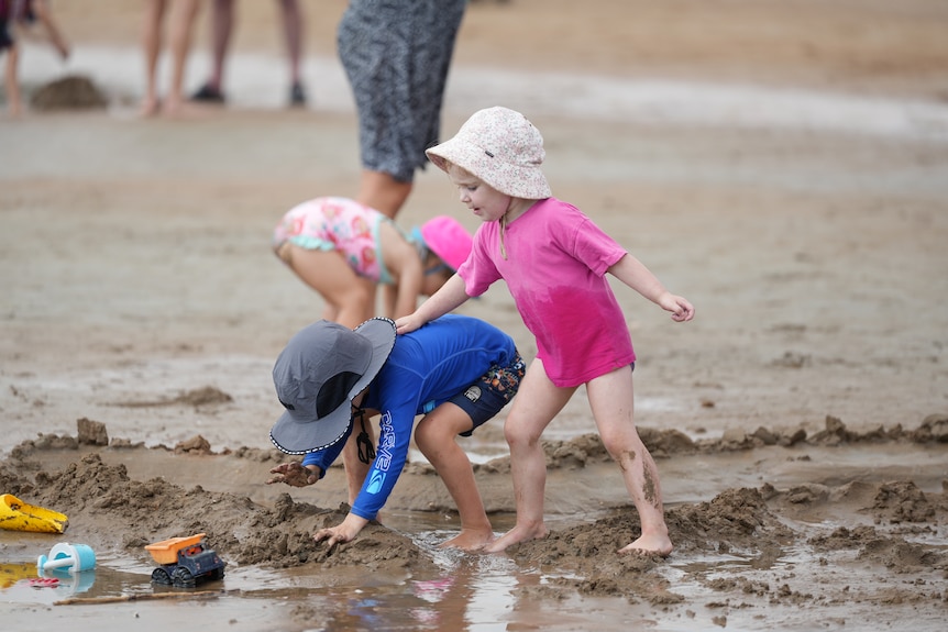 Two kids play in sand on beach 