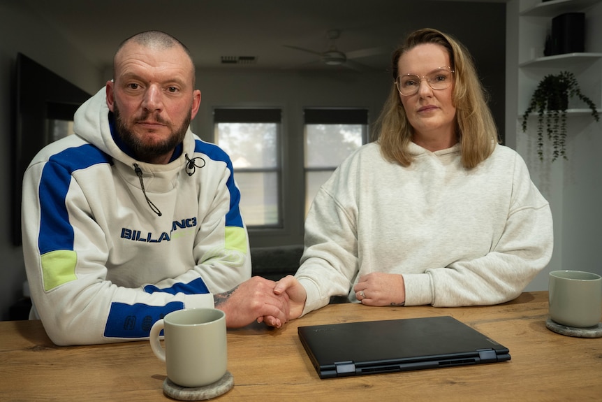 A bearded man and his midwife wife hold hands at their kitchen table in Whyalla