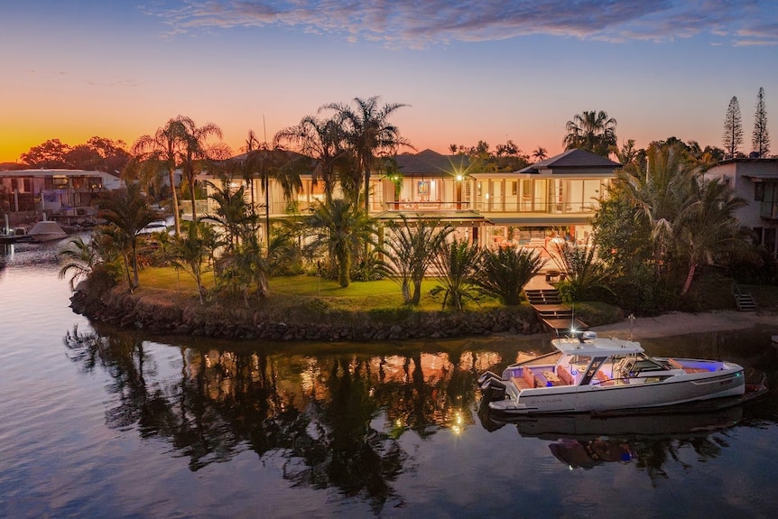 A waterfront mansion at sunset with a boat on the river