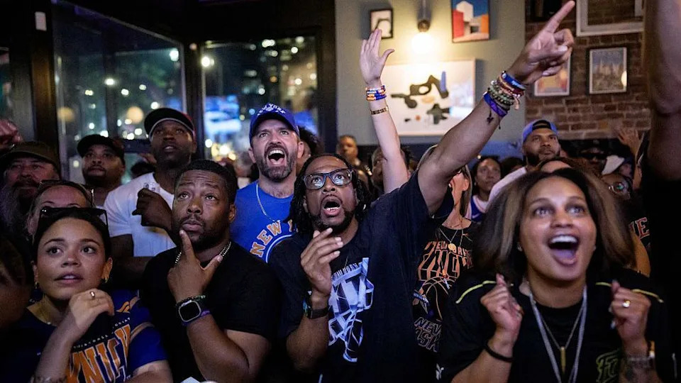 A group of cheering fans wearing Knicks gear in a bar