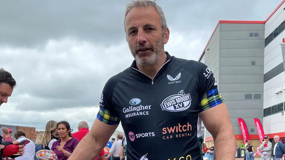 Image of a man in cycling gear. In the background can be seen a crowd of people and the outside of a large stadium building