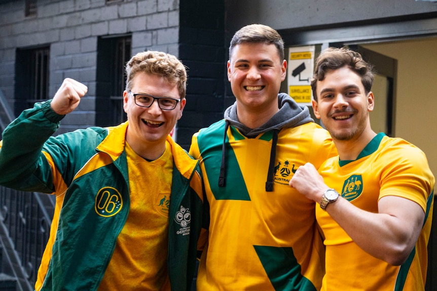 Three young men in sports gear pump their fists and cheer.