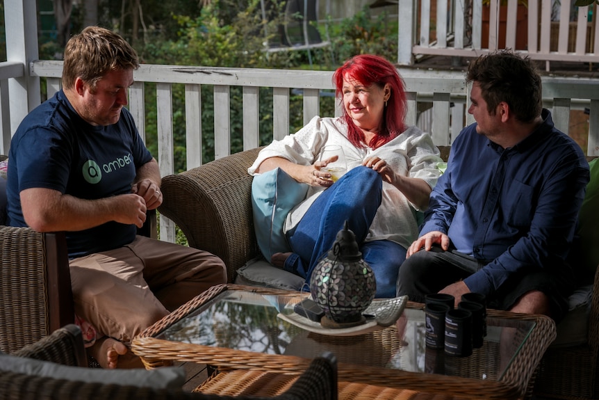 A woman sits outside between her two adult sons.