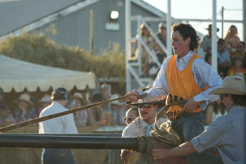 A young man particpates in an obstacle course, pulling himself along a greasy timber pole.