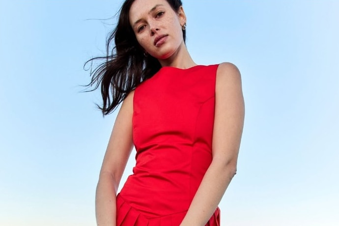 Young woman with dark hair stands outdoors wearing a bright red shift dress.