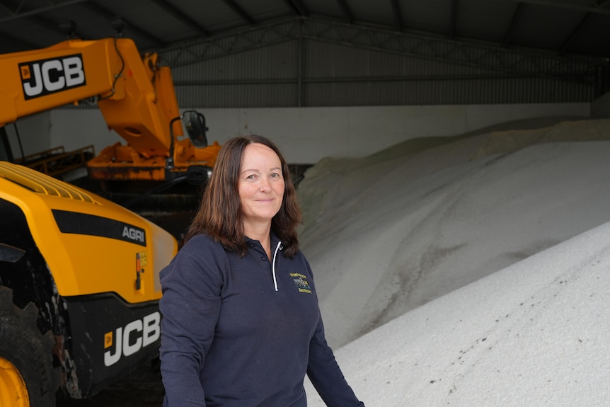 A woman on a farm stands next to a large heap of white fertiliser.