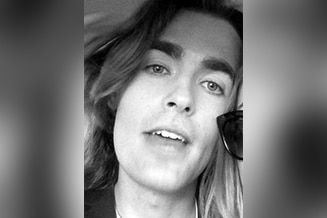 A close-up black and white selfie shot of a man with long hair.
