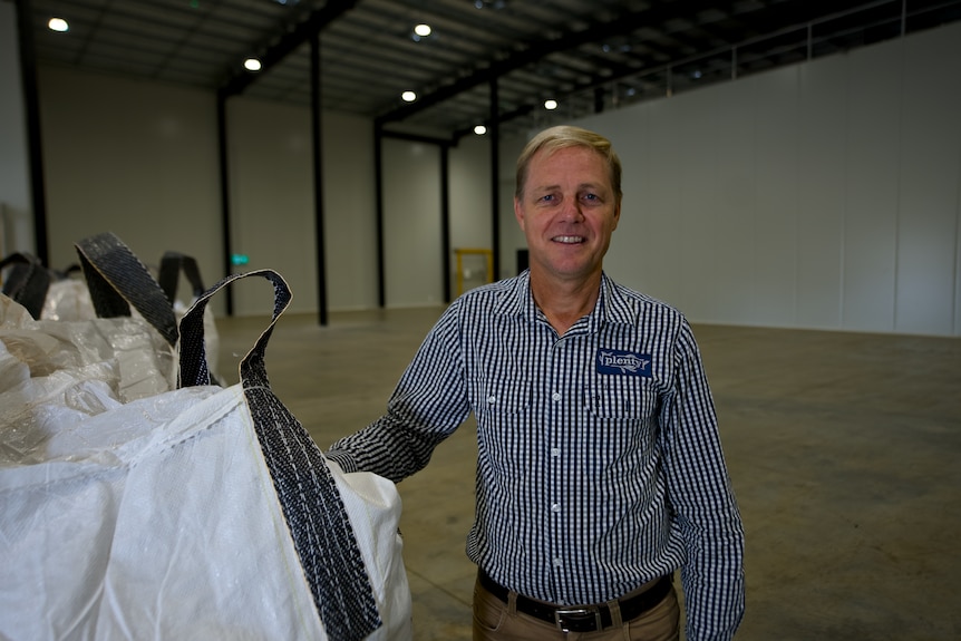 An older man standing next to large industrial bags.