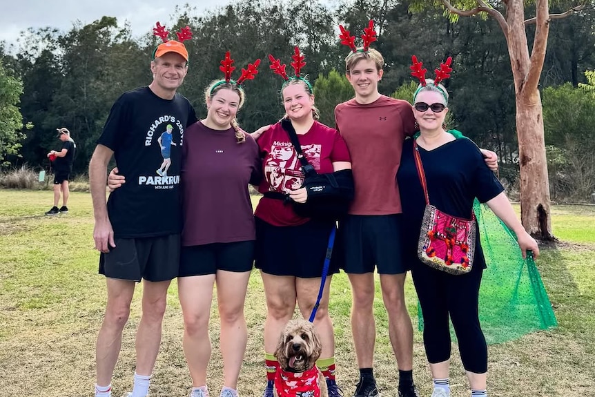 Two adults stand with their two female and one male young adult children while wearing reindeer headbands