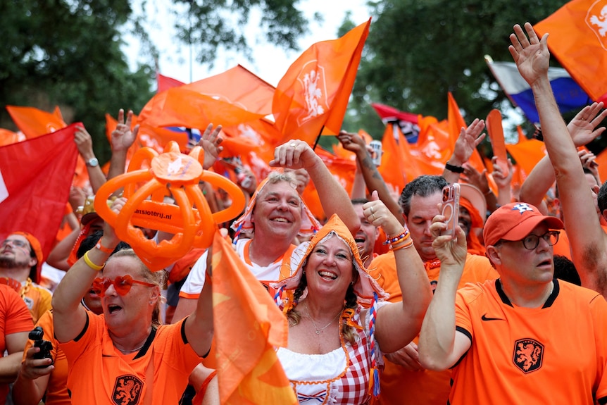 a crowd of netherlands fans dressed in orange - a man and woman in traditional dress in the centre