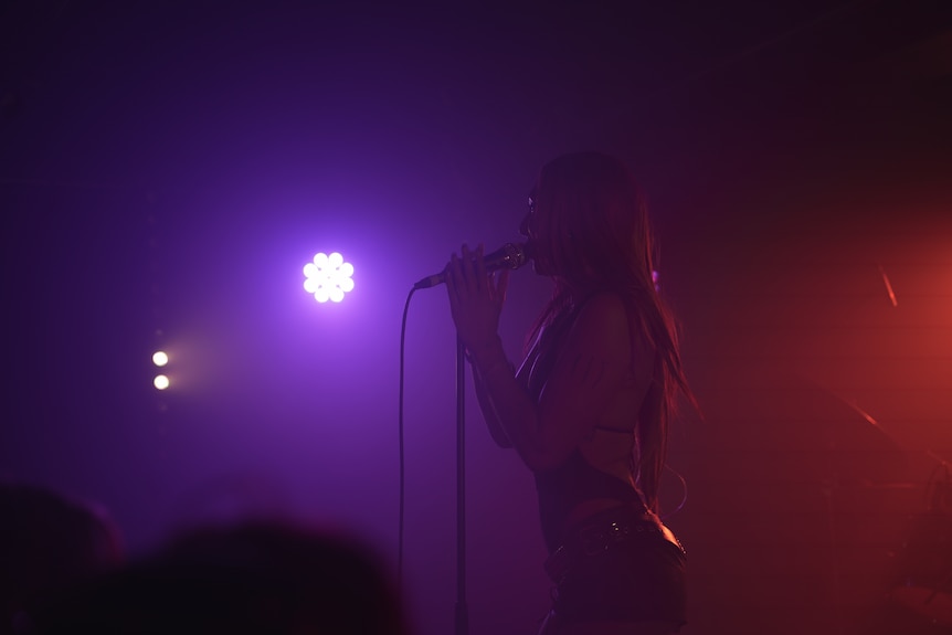 Miss Kaninna stands on stage behind a microphone.