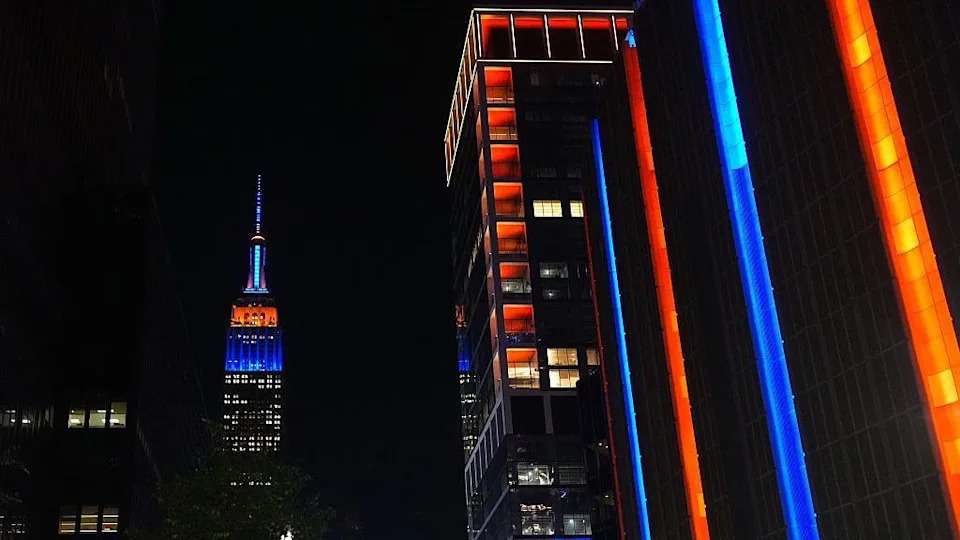 City skyscrapers lit up in orange and blue amid night sky