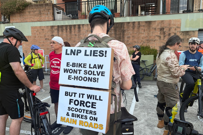 A person carrying a sign on their back while stook near a bike.