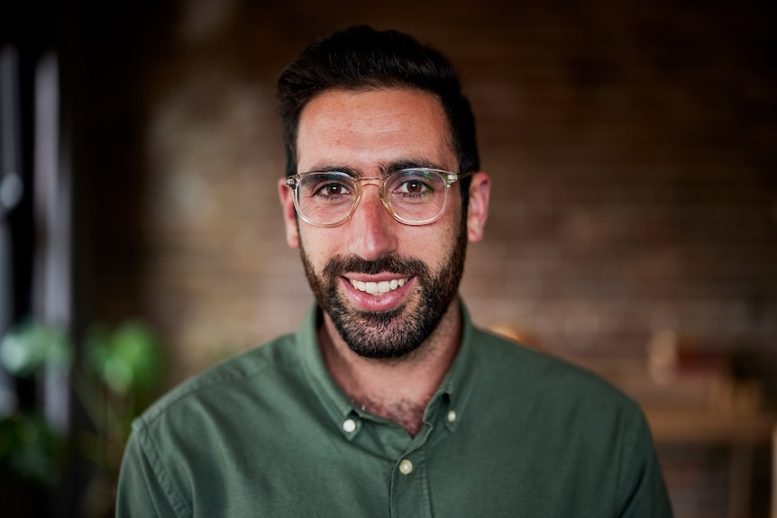 Dr Zac Seidler smiles for the camera. He is wearing reading glasses and a green shirt.
