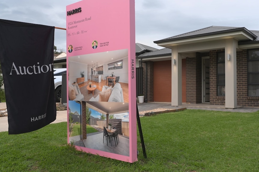 A modern house with a pink real estate sign and black Auction flag