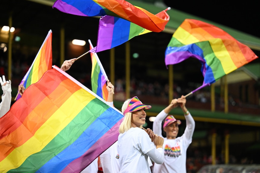 People in stands wearing white shirts and waving rainbow coloured Pride flags