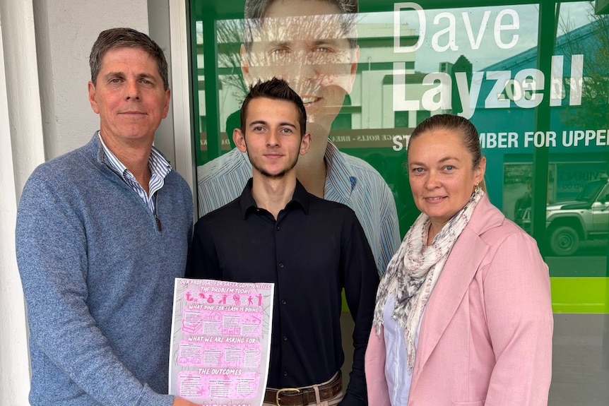 Dave Layzell stands next to a woman and a teenage boy holding a pink information sheet, outside his Singleton office